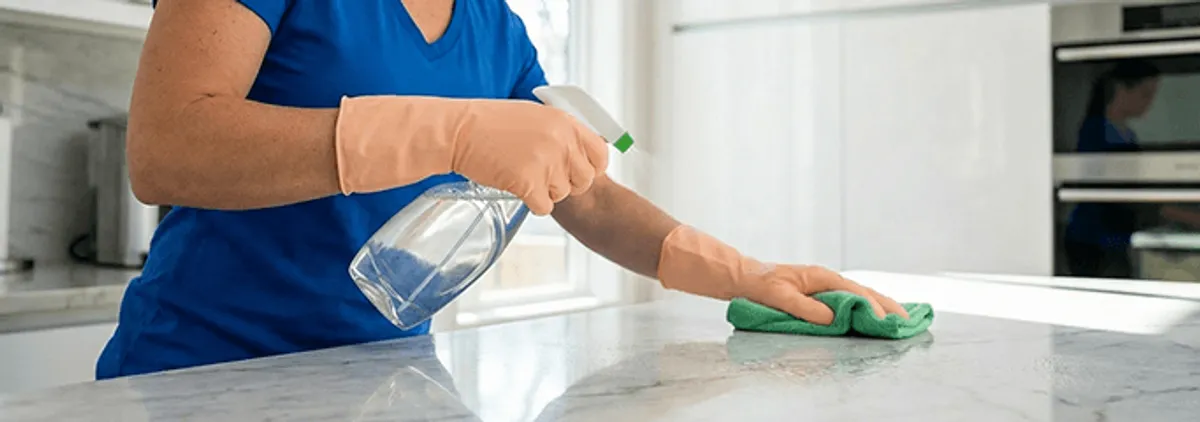 Maid service worker spraying and wiping a kitchen countertop with a microfiber cloth for sanitizing, Sacramento, CA.
